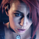A red-haired woman stares off screen with a large computer screen behind her.